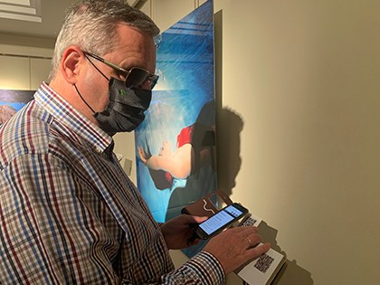 Una persona ciega utiliza su móvil para escuchar la música asignada por Inteligencia Artificial a la fotografía expuesta